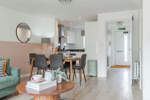 A modern living room with a dining area, a kitchen in the background, and a door marked 'Emergency exit'. - Host & Stay | Gladiator Getaway (Cambourne)