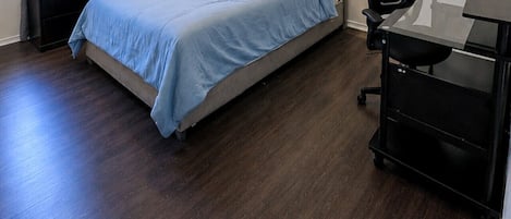 Un dormitorio con cama, escritorio, silla, ventilador de techo y ventana con cortinas.