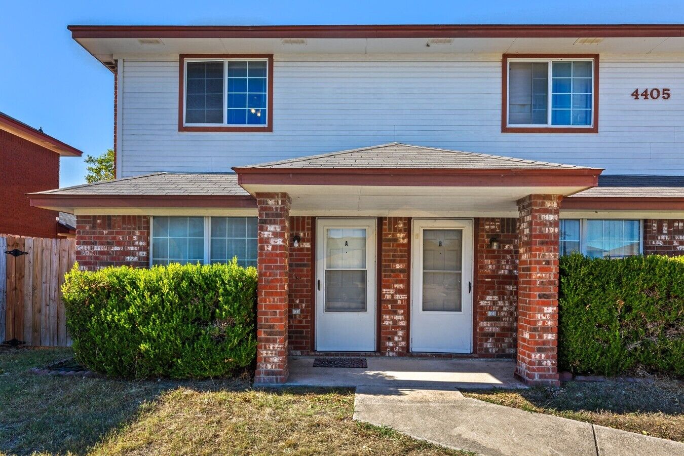 A two-story residential building with a brick facade, a front porch, and a mailbox.