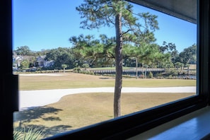 A window view of a golf course with a clear sky, a bridge, and residential buildings in the background. - New Listing! Gorgeous Golf Views 2 BR Condo Palmetto Dunes Resort (Hilton Head Island)