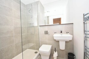 Ein modernes Badezimmer mit einer gläsernen Duschkabine, einer weißen Toilette, einem Waschbecken mit Spiegel darüber und einem Handtuchhalter.