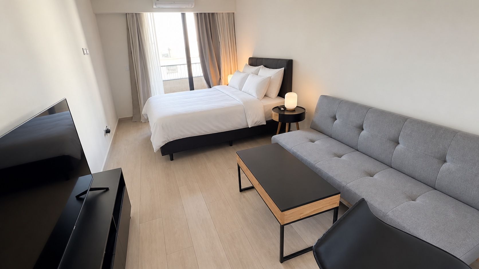 Quarto de hotel moderno com cama, sofá, mesa de centro e televisão.