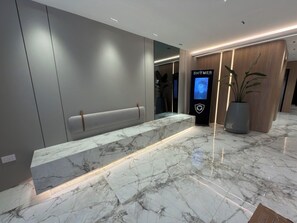 A reception area with a marble counter, a bench, a digital display, and a potted plant. - Plaza Italia: Luxury Building with Gym and Cowork (CABA)