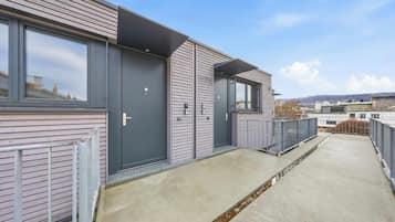 Ein modernes Gebäude mit flachem Dach, großen Fenstern und einem Betonweg, der zu einem begrenzten Eingang führt.