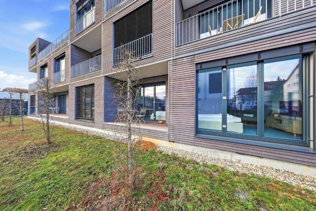 A multi-story residential building with balconies, large windows, and a well-maintained lawn.