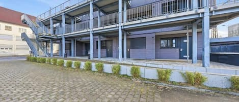 A multi-story building with a covered outdoor area, a staircase, and a paved ground.