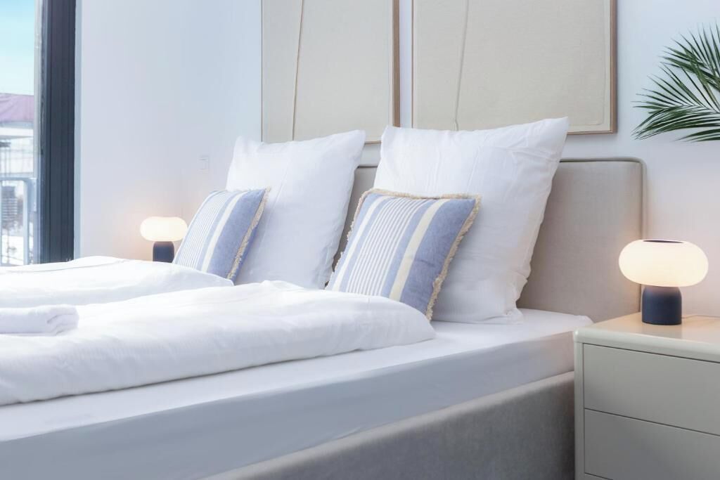 A modern hotel room with a large bed, two bedside lamps, and a city view.