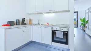 A modern kitchen with white cabinets, a built-in oven, and a countertop with a coffee maker and tomatoes. - Lunea Stay Apartment Hotel in Esslingen (Esslingen am Neckar-Mettingen)