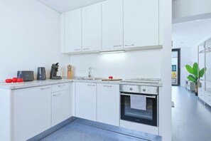 Una cocina moderna con armarios blancos, horno empotrado y una encimera con cafetera y tomates.