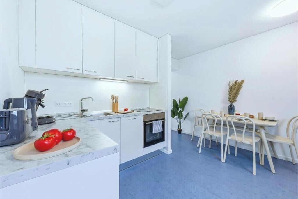 Eine moderne Küche mit weißen Schränken, einem eingebauten Backofen und einem Essbereich mit Tisch und Stühlen.