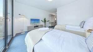 Ein Hotelzimmer mit einem großen Bett, einem kleineren Bett, einem Fernseher, einer Pflanze und Blick durch eine Glastür.