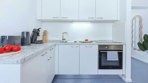 Eine kompakte Küche mit weißen Schränken, einem eingebauten Backofen und einer Arbeitsplatte mit Wasserkocher, Kaffeemaschine und Tomaten.