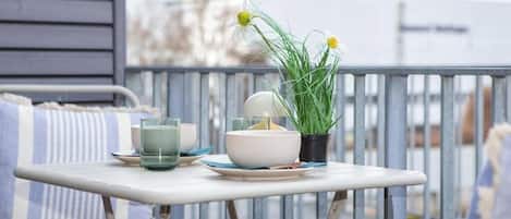 A balcony with a table set for two, featuring a bowl, glasses, and a potted plant.