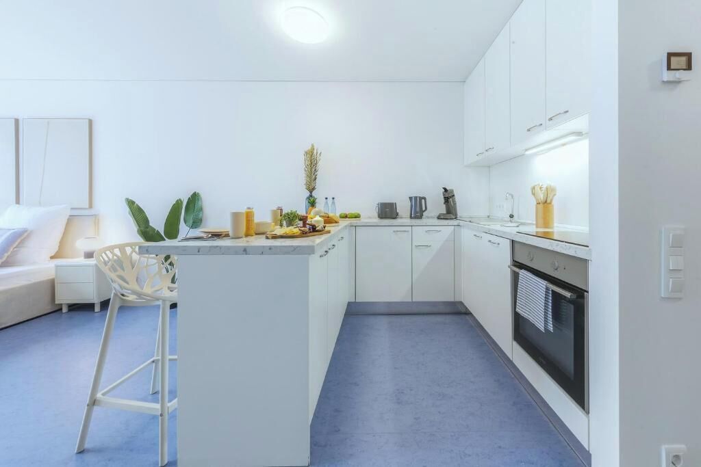 Eine moderne Küche mit weißen Schränken, einer zentralen Kochinsel und einem Barhocker.