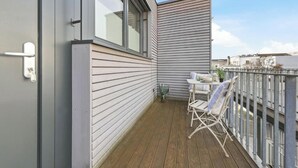 Ein Balkon mit Holzboden, einem weißen Klappstuhl und einem kleinen Tisch mit einer Pflanze.