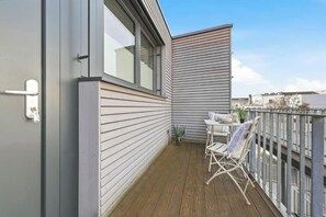 Un balcón con piso de madera, una silla plegable blanca y una pequeña mesa con una planta.