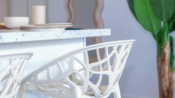 A white chair with a geometric design, a white table with a marble-like surface, and a potted plant in the background.
