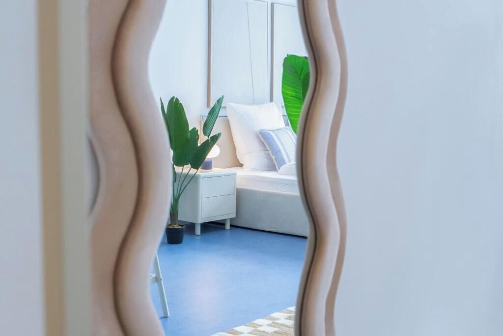 Ein Schlafzimmer mit einem weißen Bett, einem Nachttisch, einer Topfpflanze und einem großen grünen Blatt.