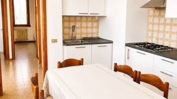 A compact kitchen with a stove, sink, and white cabinets. A dining table with chairs is positioned in front of the kitchen.