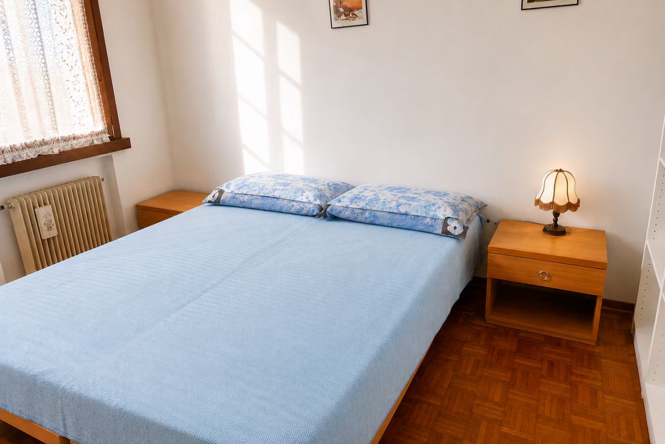 A bedroom with a bed, two pillows, a nightstand with a lamp, and a radiator.