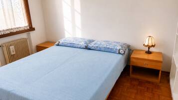 A bedroom with a bed, two pillows, a nightstand with a lamp, and a radiator.