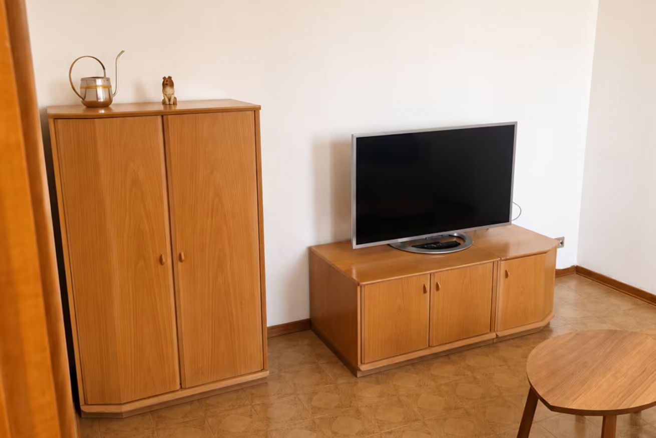 A room with a wooden cabinet, a television on top, and a small round table.