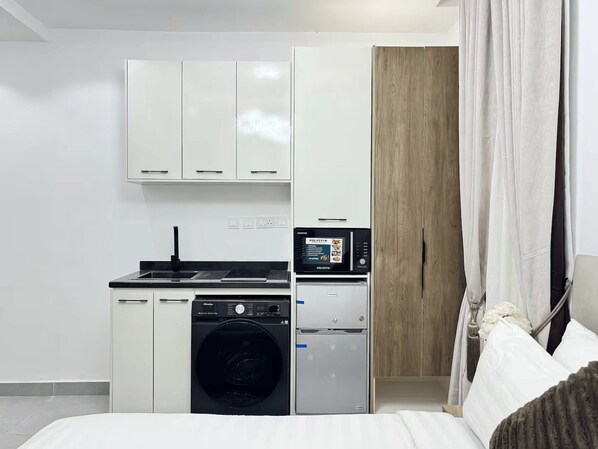 A compact kitchen with a washing machine, a small refrigerator, and a microwave. - Modern Studio Apartment in Victoria Island with Pool, Fast Wi-Fi & 24/7 Power (Lagos)