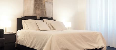 A modern bedroom with a large bed, two bedside tables, and a large abstract painting on the wall.