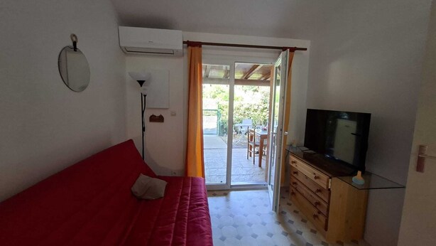 Ein Zimmer mit einem roten Sofa, einem Fernseher auf einer Holzkommode und einer Glastür zum Außenbereich.