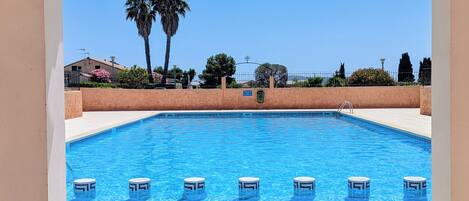 A swimming pool with clear blue water, surrounded by a tiled deck and a low wall.