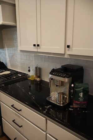A kitchen with white cabinets, a black countertop, a coffee maker, a kettle, and a bag of coffee beans.