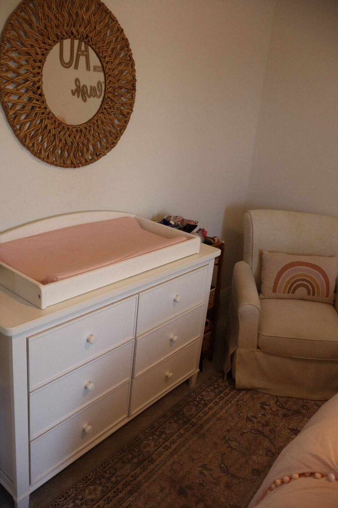 Une chambre avec un berceau, une commode blanche, un tapis à motifs et un élément décoratif mural.