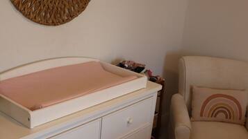 Une chambre avec un berceau, une commode blanche, un tapis à motifs et un élément décoratif mural.
