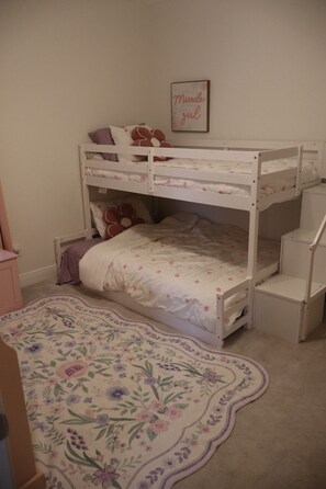 A bunk bed with a floral bedspread, a small desk, and a framed motivational quote on the wall.