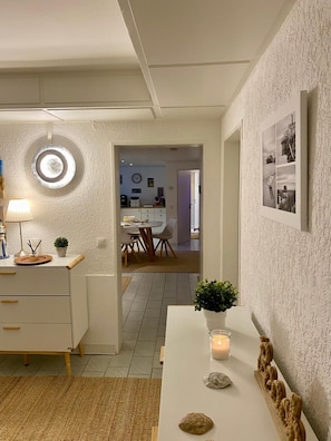 Ein modernes Interieur mit Essbereich, einem weißen Schrank mit Schubladen, einer runden Leuchte und einer Wandcollage mit Fotos.