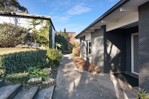 Ein Wohnhaus mit befestigter Auffahrt, einem Garten mit verschiedenen Pflanzen und einem Gebäude mit dunkler Fassade und einem Fenster.