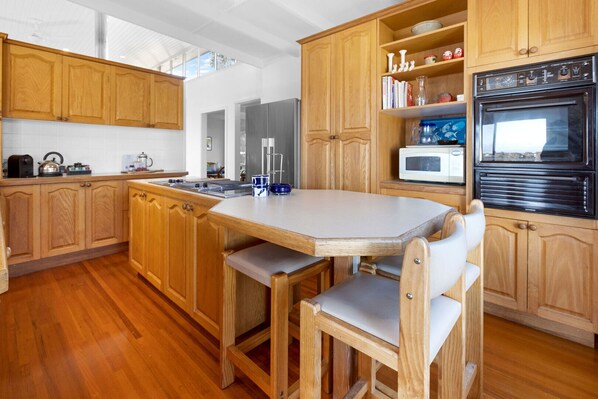 Eine moderne Küche mit Holzausstattung, einer zentralen Kochinsel mit Sitzgelegenheiten, einer Mikrowelle und einem Backofen.