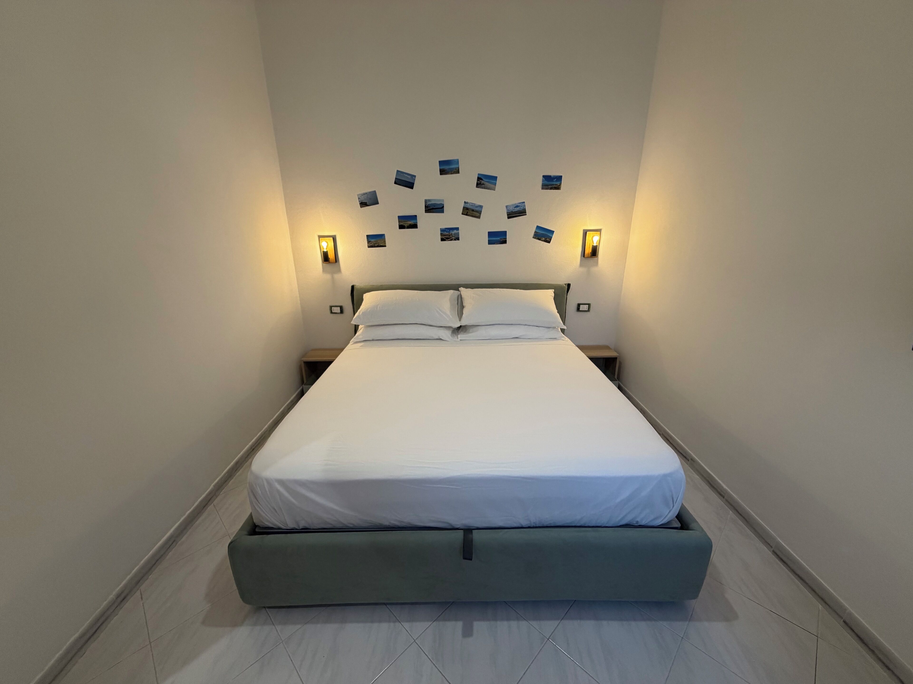 A hotel room with a single bed, two bedside tables, and wall-mounted picture lights.