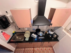 Eine kleine Küche mit weiß gefliestem Fliesenspiegel, einer schwarzen Arbeitsplatte und rosa Schränken.