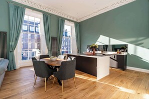 A modern kitchen with a central island, dining area with chairs, and large windows with curtains. - Fleming Suite - 2 Bed Luxury Apartment (Edinburgh)