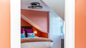 Un dormitorio con techo inclinado, una cama con muchos almohadones, una lámpara de noche y un radiador.