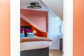 Ein Schlafzimmer mit schrägem Dach, einem Bett mit vielen Kissen, einer Nachttischlampe und einer Heizung.