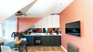 Una cocina moderna con comedor, televisor montado en la pared y un amplio ventanal que proporciona luz natural.