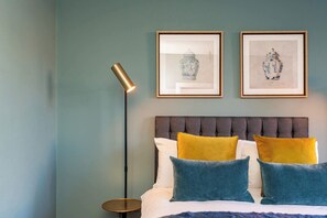 Ein Schlafzimmer mit einem Bett, einer Stehlampe und zwei gerahmten Kunstwerken an der Wand.