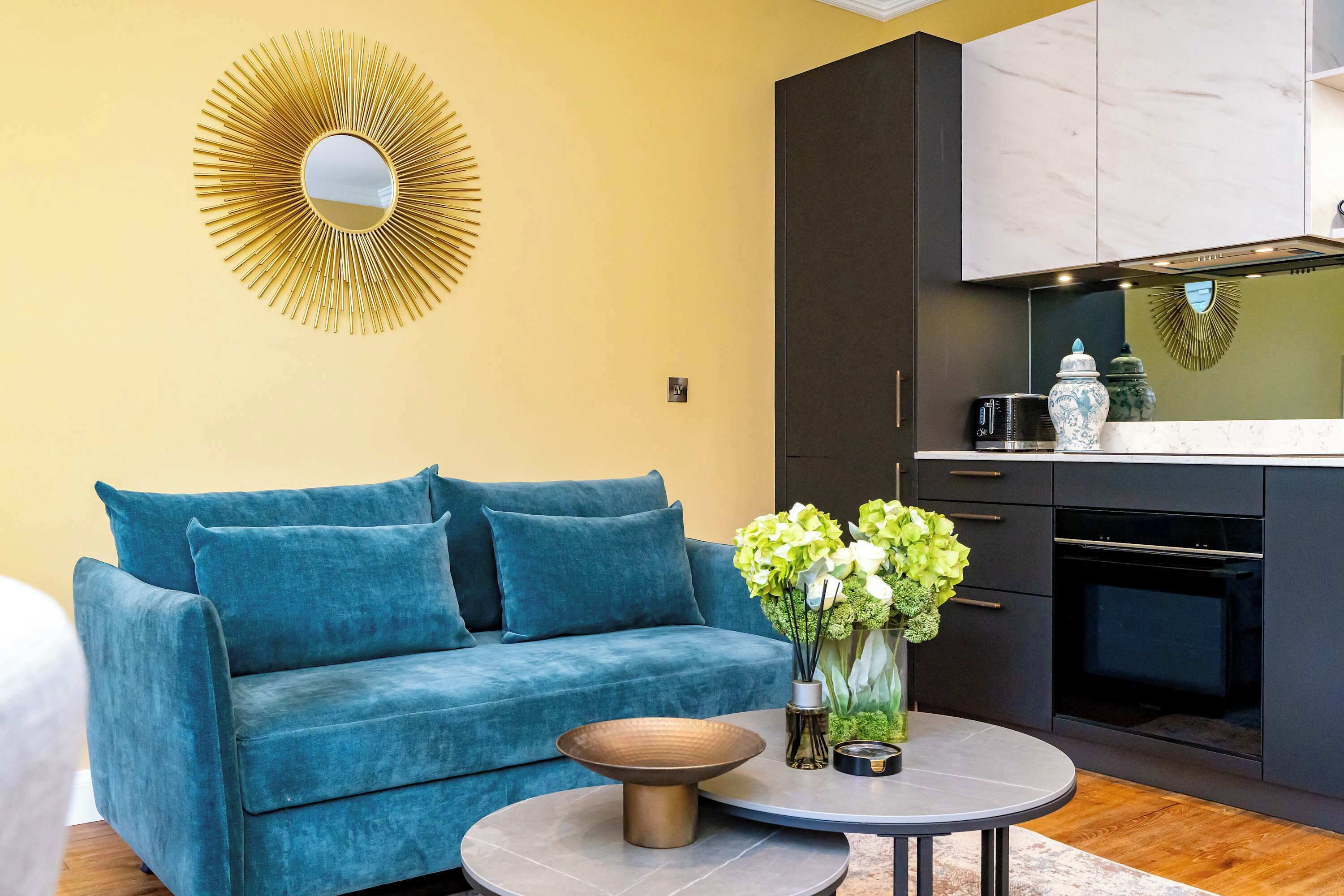 A modern living room with a blue sofa, a round coffee table, and a decorative mirror on the wall.