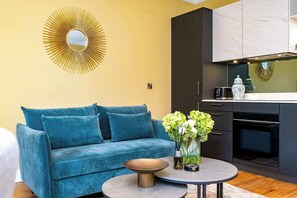 A modern living room with a blue sofa, a round coffee table, and a decorative mirror on the wall. - Bain Suite - 1 Bed Luxury Apartment (Edinburgh)