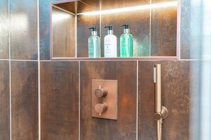 A bathroom with a shower area, a shelf with toiletries, and a control panel. - Bain Suite - 1 Bed Luxury Apartment (Edinburgh)