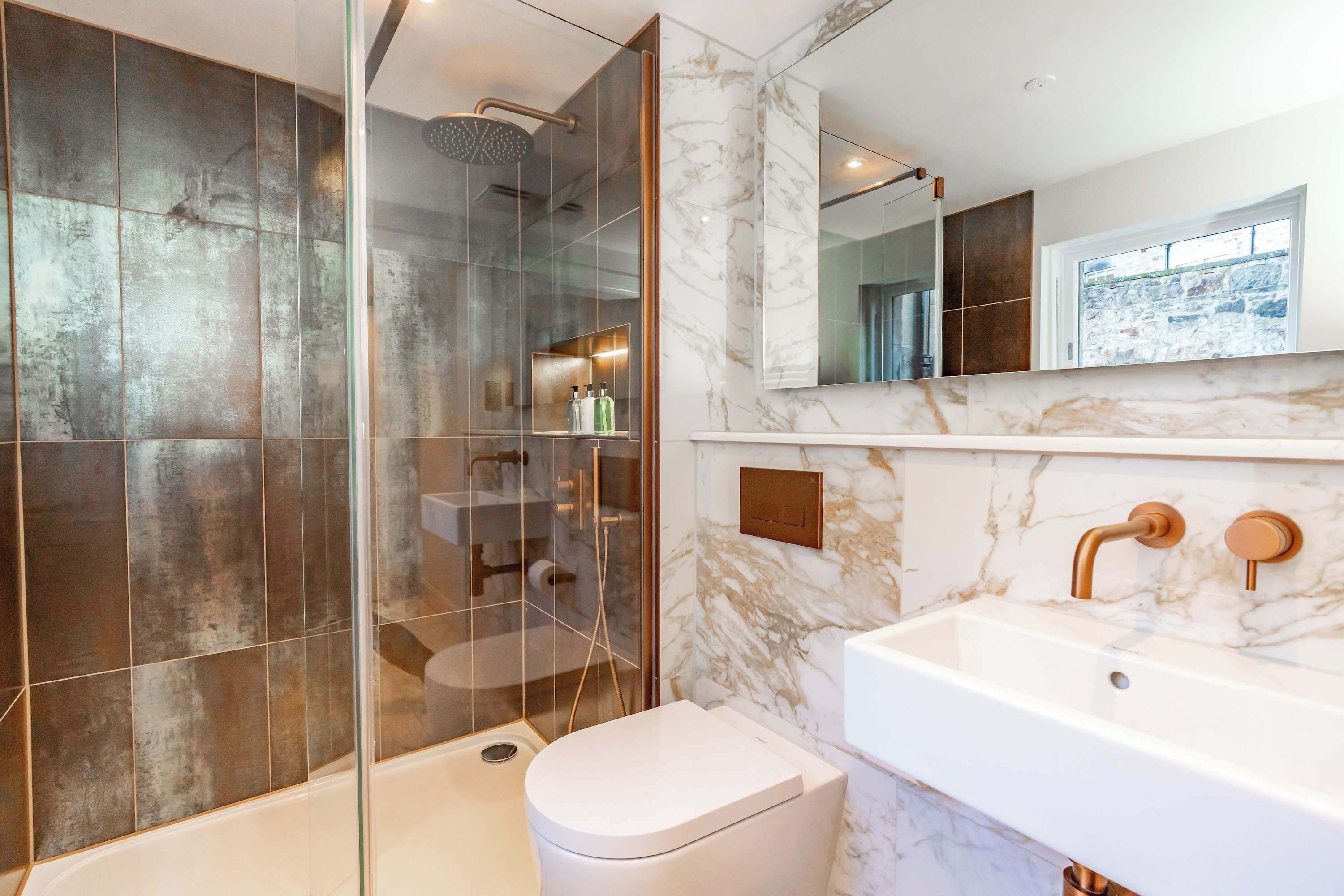 A modern bathroom with a glass-enclosed shower, a white toilet, and a marble-tiled sink area.