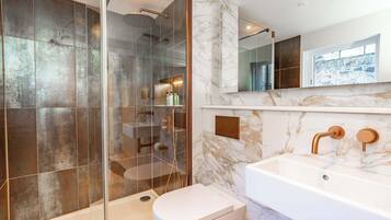 A modern bathroom with a glass-enclosed shower, a white toilet, and a marble-tiled sink area.