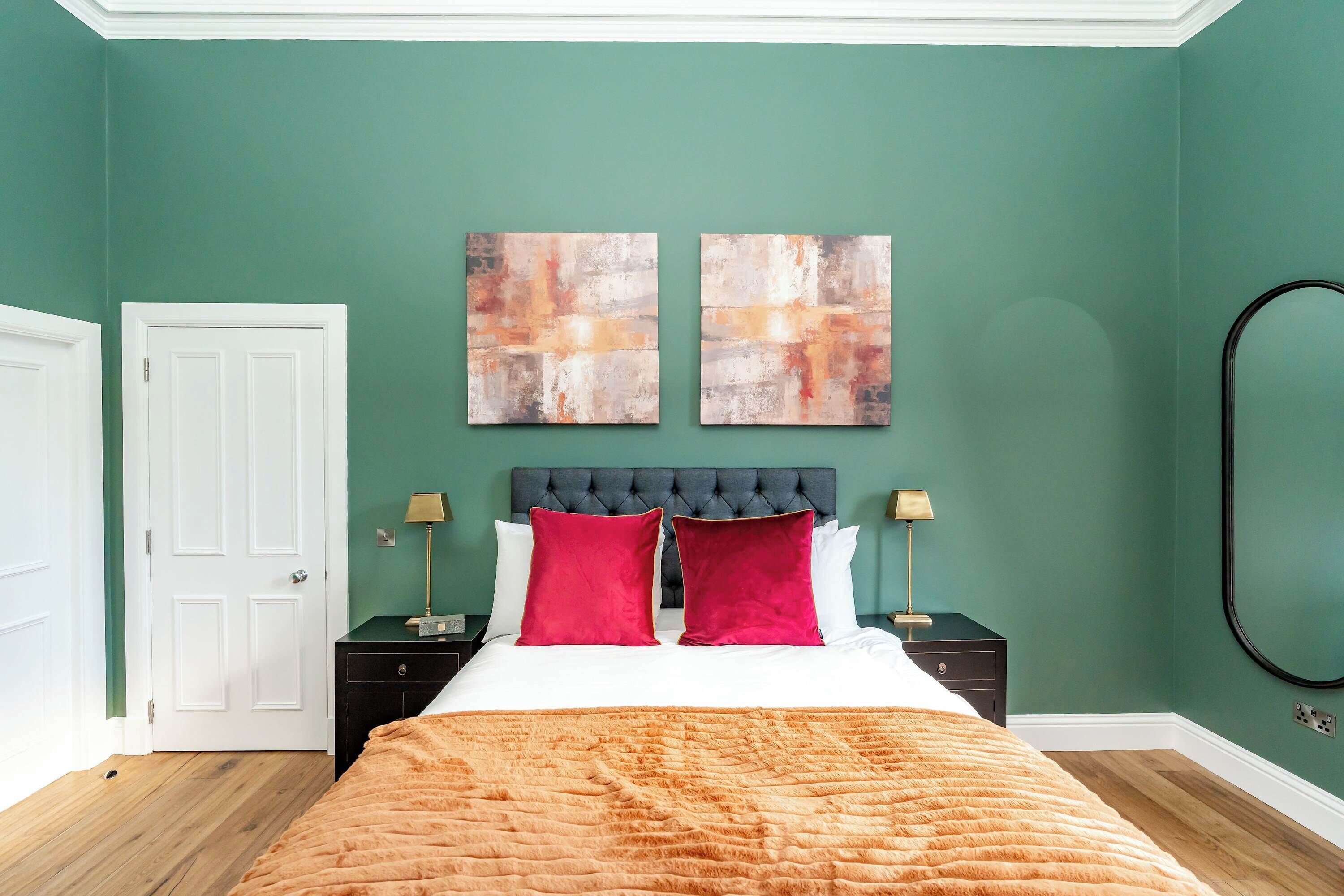 A bedroom with a bed, two bedside tables, a headboard, and two abstract paintings on the wall.